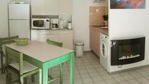 A compact kitchen with a dining table, chairs, a microwave, a coffee maker, a washing machine, and a painting on the wall.