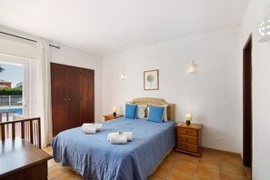 A bedroom with a bed, bedside tables, a wardrobe, and a view of a pool.