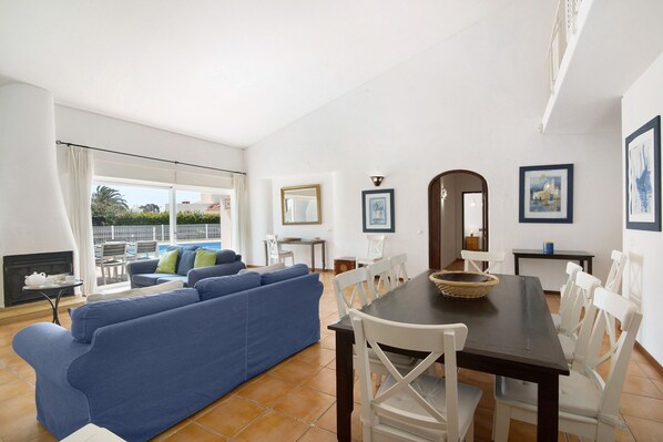 A living room with a blue sofa, white dining chairs, a dark wooden table, and a fireplace.