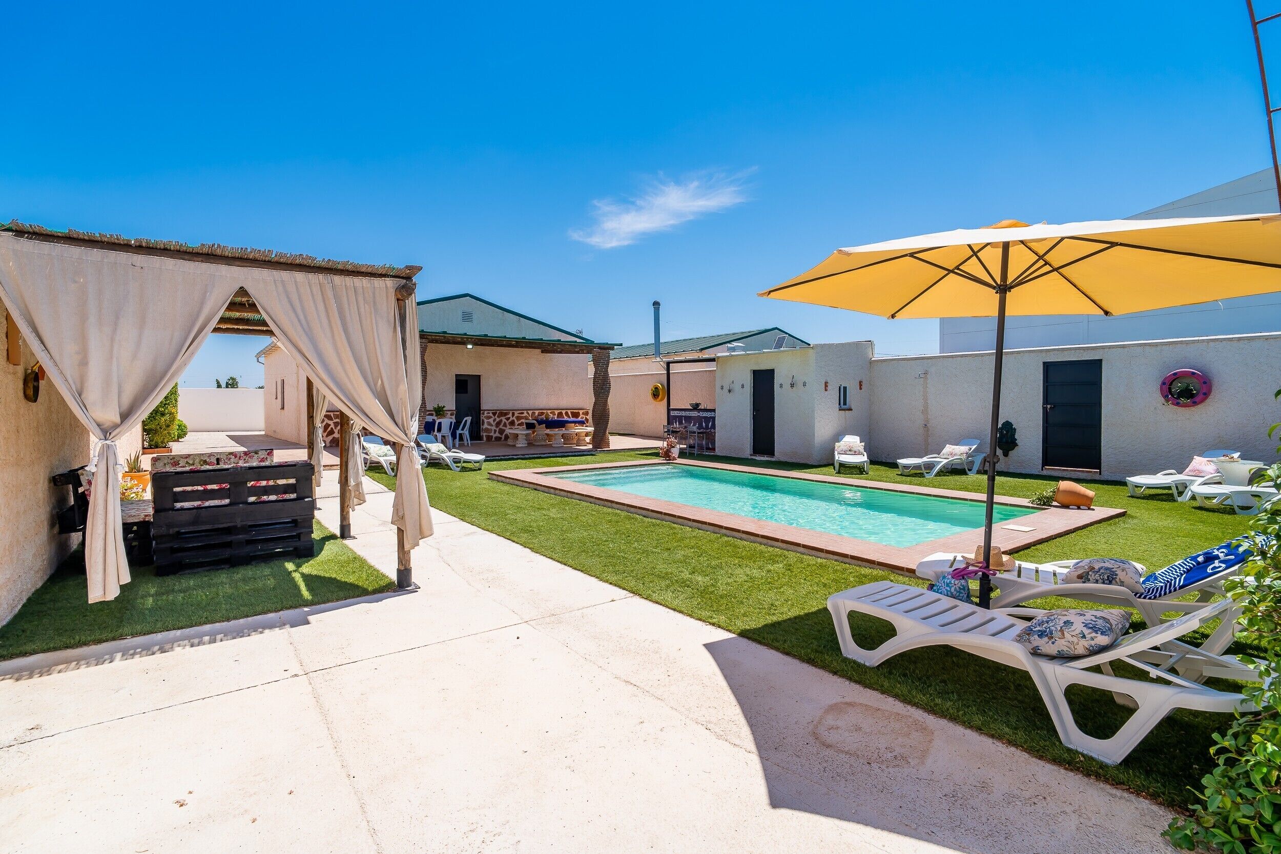 A pool area with lounge chairs, a pergola, and a covered seating area.