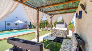 Una terrazza esterna con piscina, mobili in legno e una zona coperta con tetto di paglia.