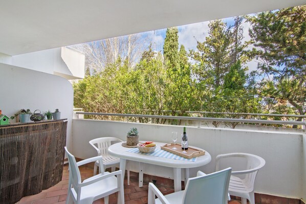 A balcony with a table, chairs, a small grill, and potted plants.