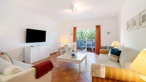 A living room with a television, sofa, coffee table, and a dining area with chairs and a table. - Apartment 'Prainha Paradise - Algarve' with Shared Pool, Wi-Fi and Air Conditioning (Alvor)