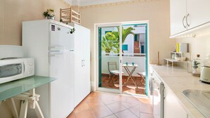 A compact kitchen with a refrigerator, microwave, and a glass-top table. - Apartment 'Prainha Paradise - Algarve' with Shared Pool, Wi-Fi and Air Conditioning (Alvor)