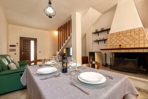 Un coin repas avec une table dressée pour quatre personnes, un canapé vert, une cheminée et un escalier.
