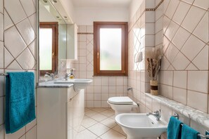 Une salle de bain comprenant un lavabo, un bidet et des toilettes, un miroir et une fenêtre.