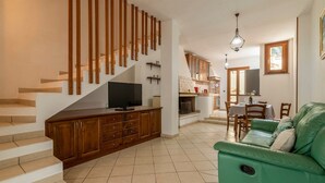 Un salon avec un canapé vert, un escalier en bois et un téléviseur posé sur un meuble.