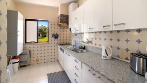 Una cocina compacta con gabinetes blancos, encimera de granito, ventana con vistas y salpicadero de azulejos.
