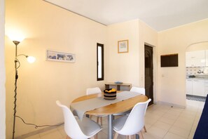 Uma sala de jantar com mesa, cadeiras, um abajur e uma cozinha ao fundo.