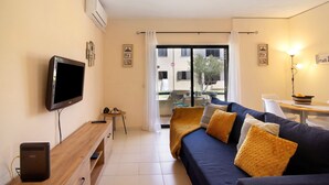 Una sala moderna con una televisión de pantalla plana, un mueble de televisión de madera, un sofá con cojines, una mesa de comedor y un balcón con vistas.