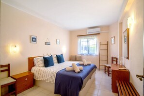 Quarto com cama, mesas de cabeceira, cadeira, escrivaninha e janela.
