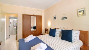 Una habitación de hotel con una cama, un armario de madera, un espejo, una mesita de noche y una lámpara fijada a la pared.