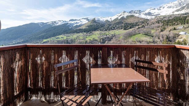 Un balcón con mesa y sillas, con vista a un paisaje montañoso y picos nevados.