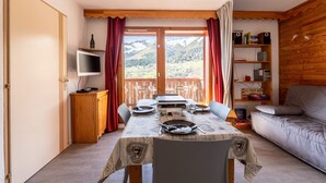 Un comedor con una mesa dispuesta para dos personas, un televisor, una estantería y un sofá.