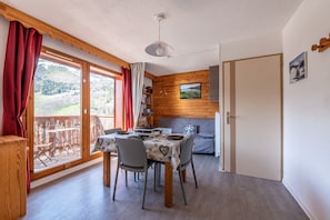 Een eetgedeelte met een tafel voor vier personen, een houten wand, een schuifdeur naar een balkon en uitzicht op een bergachtig landschap.
