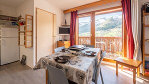 Un comedor con una mesa preparada para dos personas, un televisor sobre un mueble y vistas a montañas a través de un amplio ventanal.