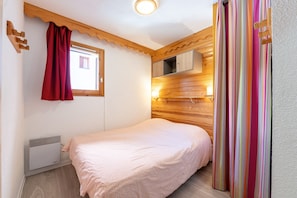 Een slaapkamer met een bed, een raam met gordijnen, een inbouwkast en een wandradiator.