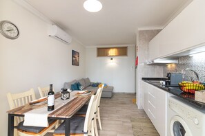 A compact kitchen with a washing machine, a dining area with a wooden table, and a living area with a sofa.