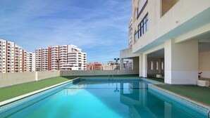 Une piscine à l’eau d’un bleu cristallin, entourée d’un immeuble doté de balcons et offrant une vue sur d’autres gratte-ciel.