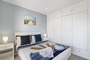 A neatly made bed with a headboard, a nightstand with a lamp, a large wardrobe, and a wall-mounted picture. - Apartment 'Luxury Beach View - Praia Da Rocha' with Sea View, Wi-Fi and Air Conditioning (Portimão)