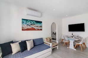 A living room with a sofa, a dining table with chairs, a flat-screen TV, and a painting on the wall. - Apartment 'Luxury Beach View - Praia Da Rocha' with Sea View, Wi-Fi and Air Conditioning (Portimão)