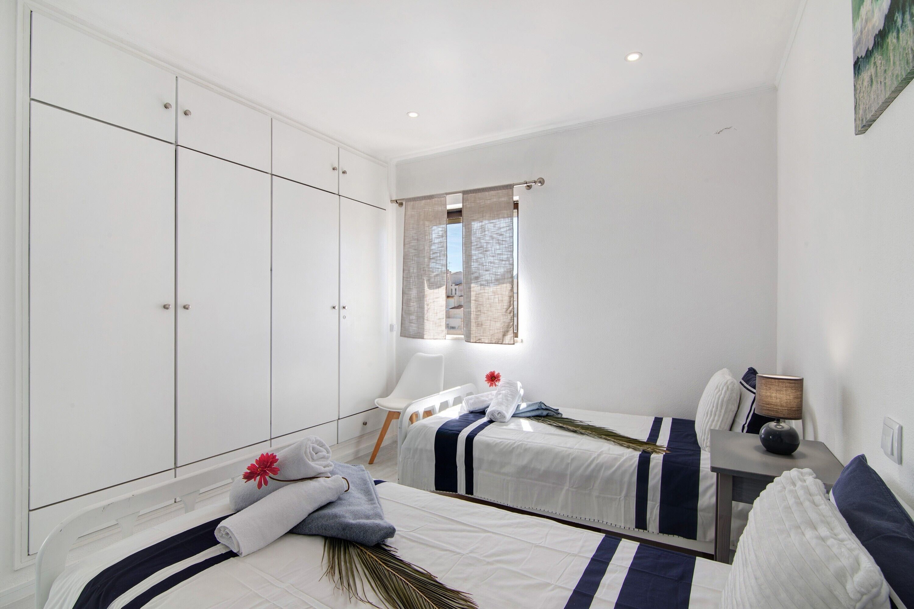 Een slaapkamer met twee bedden, een garderobe, een bureau en een raam met gordijnen.