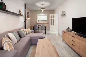 A modern living room with a sofa, coffee table, TV, wooden cabinet, and a dining area with chairs and a table.