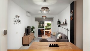 A modern living room with a wooden dining table, a sofa, a bicycle decoration, and a view to the outside. - Apartment 'Experiencia Marina A107' with Sea View, Wi-Fi and Air Conditioning (Torrox)