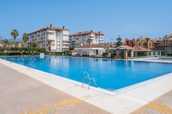 A swimming pool with clear blue water, surrounded by a tiled deck.