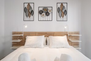 A modern bedroom with a wooden slatted headboard, white bedding, and three wall-mounted artworks.