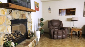 Ein Wohnzimmer mit Kamin aus Stein, einem Ledersessel, einem kleinen Tisch mit Lampe und einem wandmontierten Spiegel.
