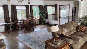 Ein geräumiges Wohnzimmer mit einer großen Couch, einem Esstisch mit Stühlen und einer Schiffslenken-Dekoration an der Wand.