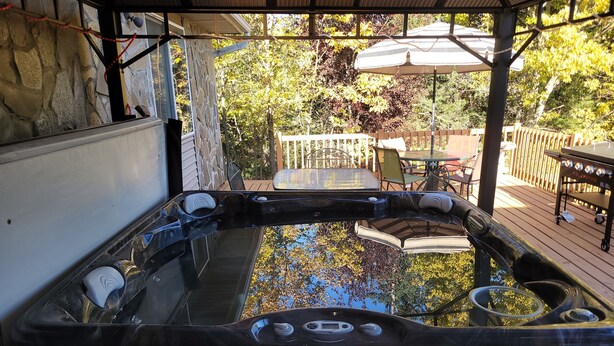 Un jacuzzi con pared de piedra y cubierta de madera, rodeado de mobiliario exterior y una valla de madera.