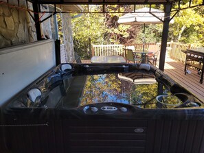Un jacuzzi con pared de piedra y cubierta de madera, rodeado de mobiliario exterior y una valla de madera.