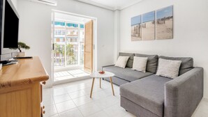 Un salon moderne avec un canapé gris, une petite table ronde et un téléviseur posé sur un meuble en bois.
