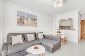 Un salon moderne avec un canapé d’angle gris, une table basse blanche et un coin repas comprenant une table et des chaises blanches.