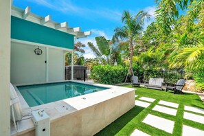 Ein moderner Poolbereich mit rechteckigem Pool, einer Betonplattform und einer Sitzecke mit zwei Stühlen und einem Tisch.