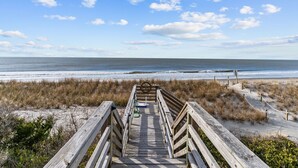 Ein Holzsteg führt zu einem Strand mit freiem Blick auf das Meer und den Himmel.
