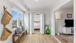 Ein modernes Interieur mit einer hölzernen Bank, gewebten Körben, einer grünen Vase, einem Bett und einem Fernseher.