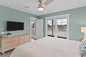A bedroom with a large bed, a flat-screen TV, a ceiling fan, a wooden dresser, and a view of a pool through a sliding glass door.