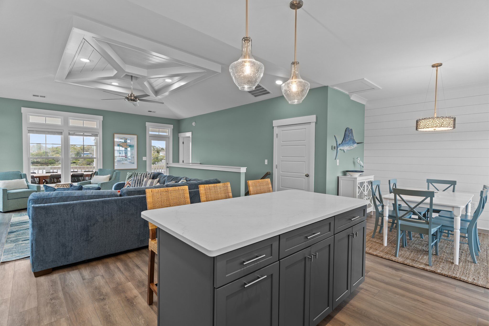 Une cuisine moderne dotée d’un îlot central, de meubles de rangement aux couleurs sombres et d’un coin repas avec des chaises bleues et une table blanche.