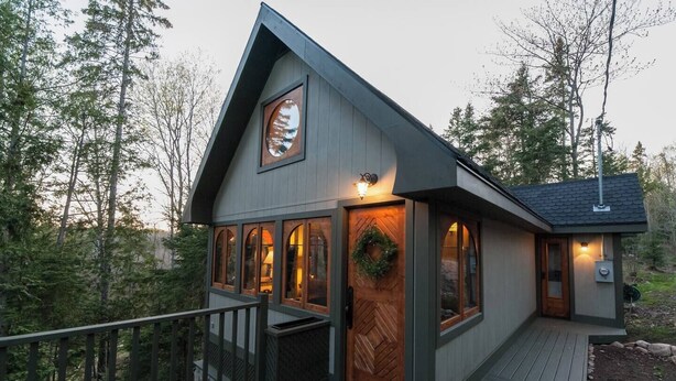 A cabin with a wooden deck, large windows, and a decorative wreath on the door.