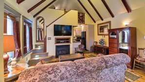 A spacious living room with a high ceiling, a fireplace, a television, and a staircase leading to an upper level.