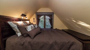 A bedroom with a large bed, a nightstand, a window with curtains, and a headboard with lights.