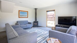 A living room with grey sofas, a TV, a fireplace, and a large window. - Kings Little Secret four bedroom family home (Wānaka)