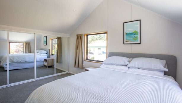 A bedroom with a large bed, a mirror, a window with curtains, and a framed picture on the wall. - Kings Little Secret four bedroom family home (Wānaka)