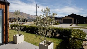 A modern residential area with a house featuring a garage, a well-maintained lawn, and a mountain backdrop. - Modern family home with mountain views (Wānaka)