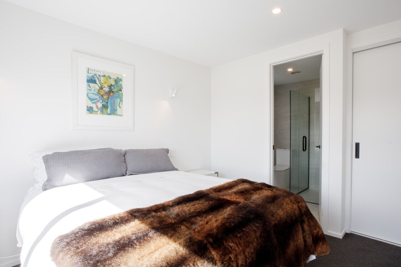 A bedroom with a large bed, a fur throw, a framed artwork, and a glass shower door.