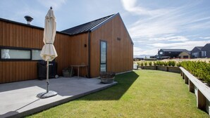 A modern building with a wooden exterior, a large umbrella, and a well-maintained lawn. - Modern family home with mountain views (Wānaka)