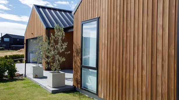 A modern building with wooden siding and large windows. - Modern family home with mountain views (Wānaka)